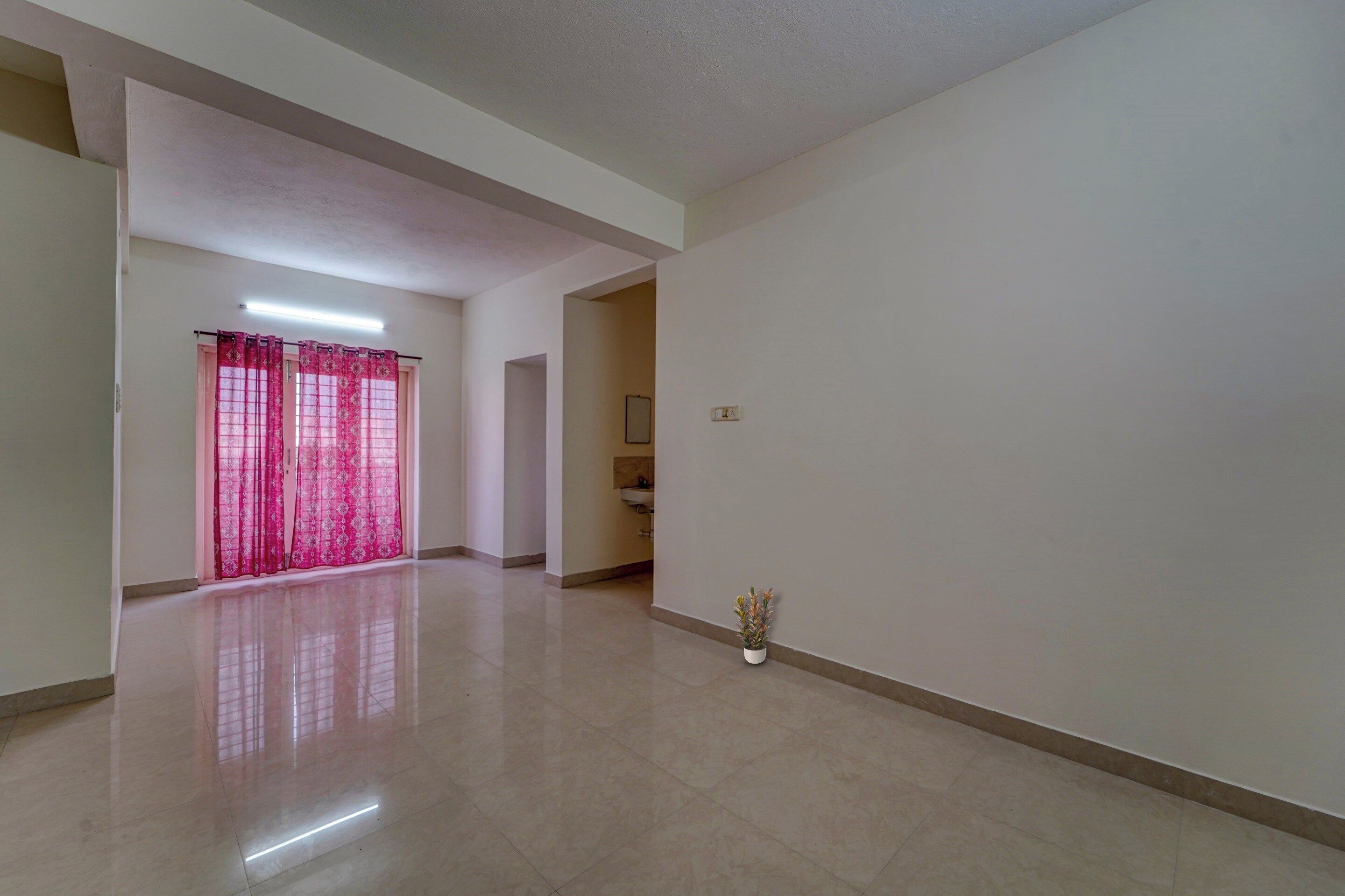 A spacious hallway with a tiled floor, a door with pink curtains, and a small potted plant.