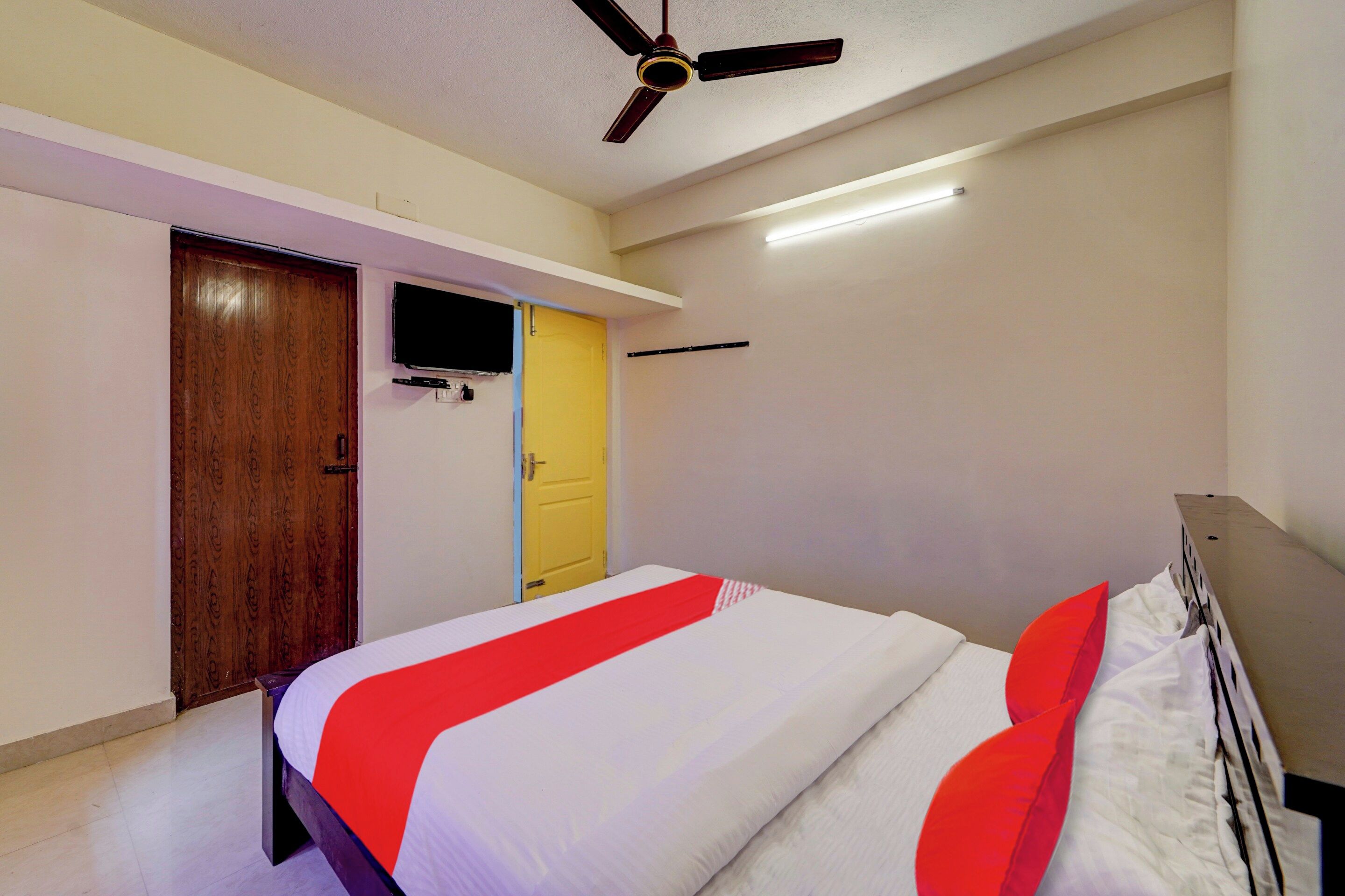 A bedroom with a bed, a ceiling fan, a TV mounted on the wall, and a door.
