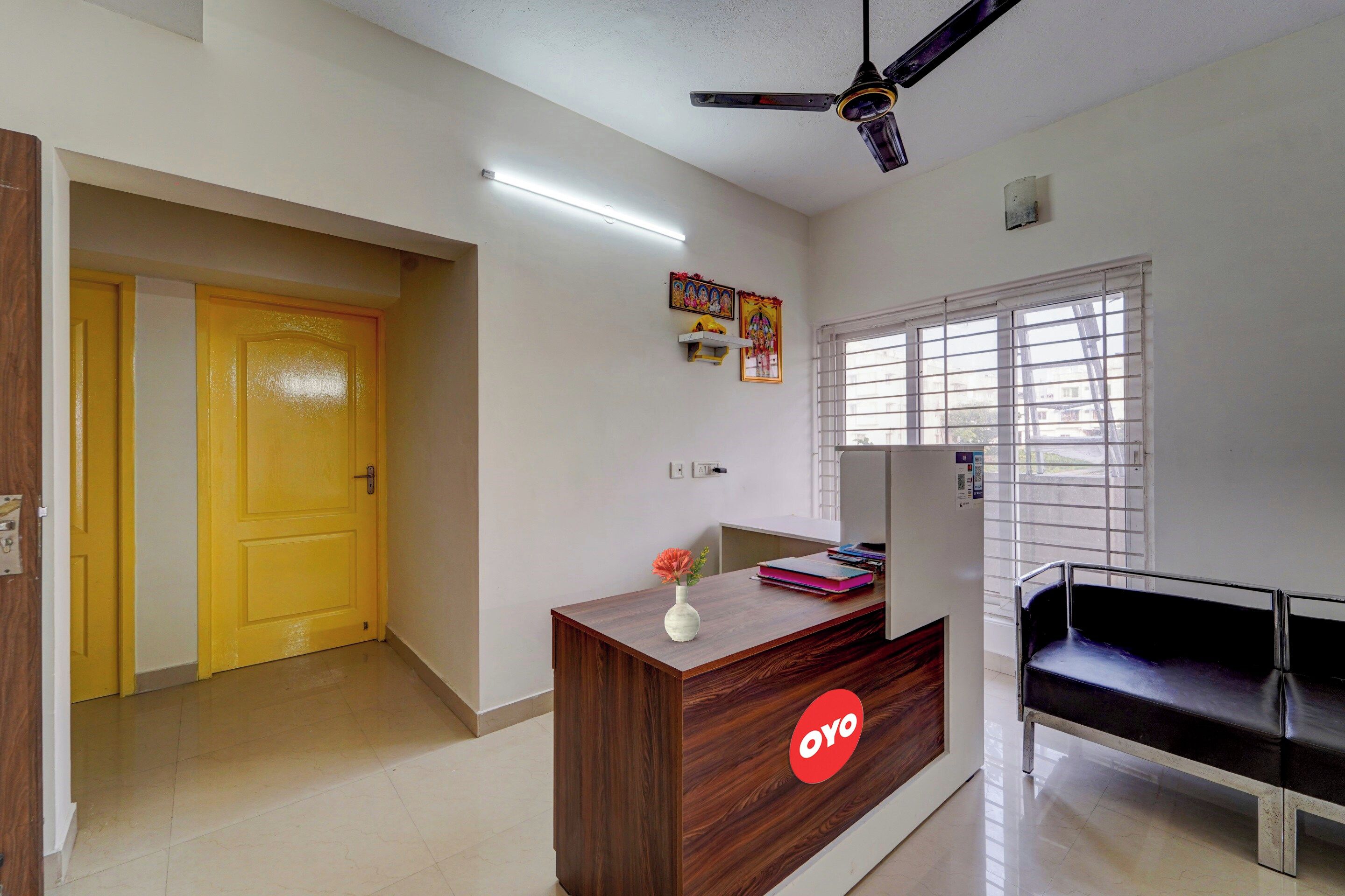 A reception desk with a logo, a window with blinds, a ceiling fan, and a door.