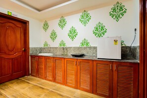 A kitchen with wooden cabinets, a white refrigerator, and decorative green wall stickers. - Hotel O Signature Grande (Pondicherry)