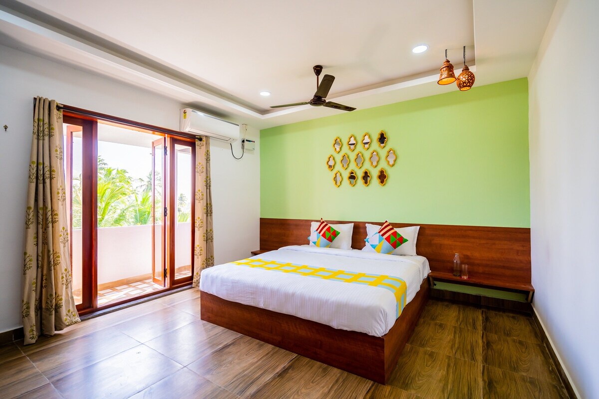 Habitación de hotel con cama, ventilador de techo, pared verde y vistas por la puerta.