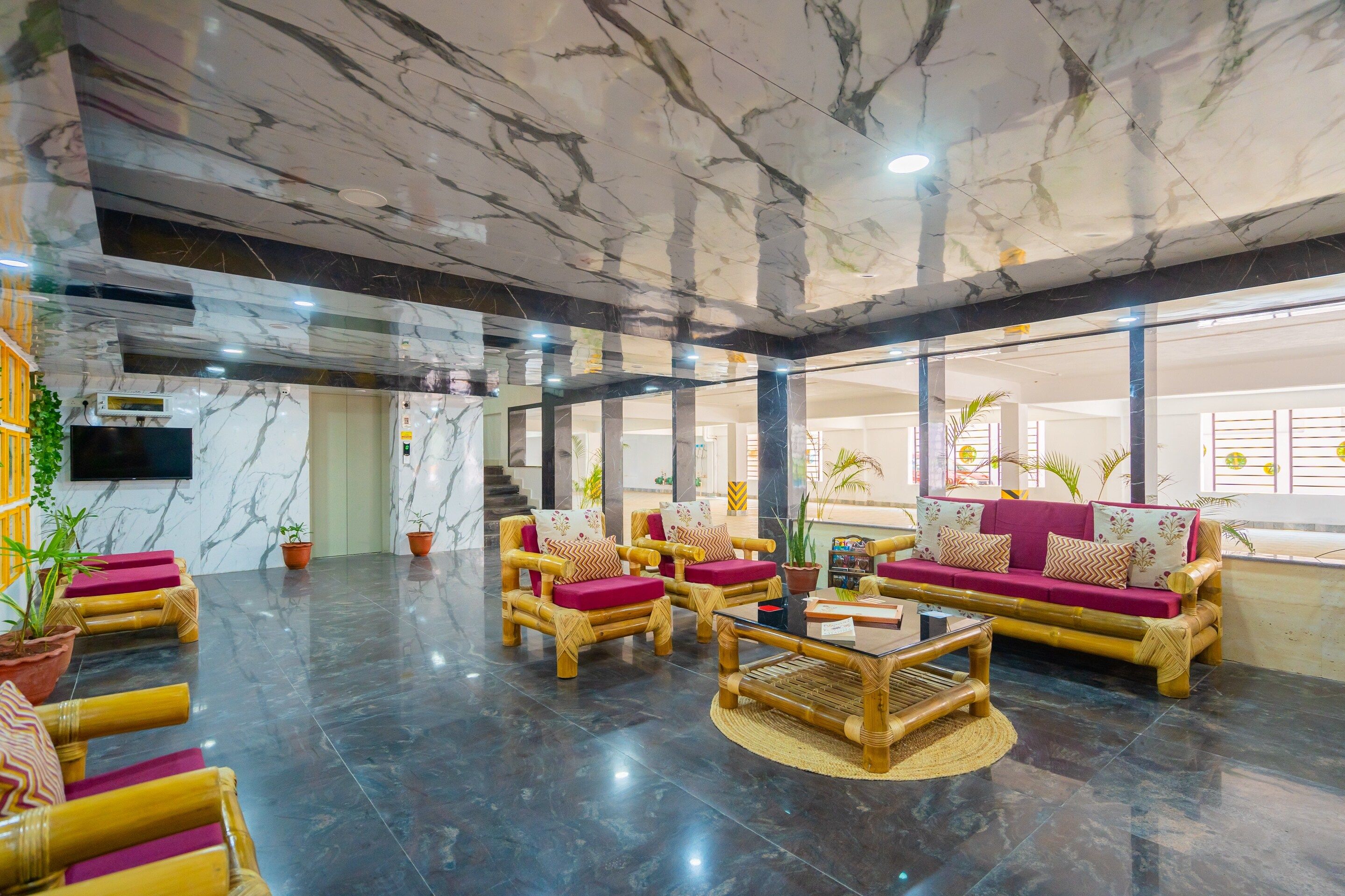 A spacious lobby with marble flooring, a sofa set, and a television mounted on the wall.