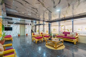 A spacious lobby with marble flooring, a sofa set, and a television mounted on the wall.