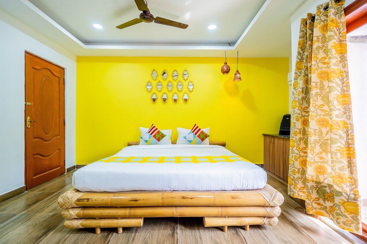 Une pièce avec un lit, un ventilateur de plafond, une porte en bois et un mur jaune.