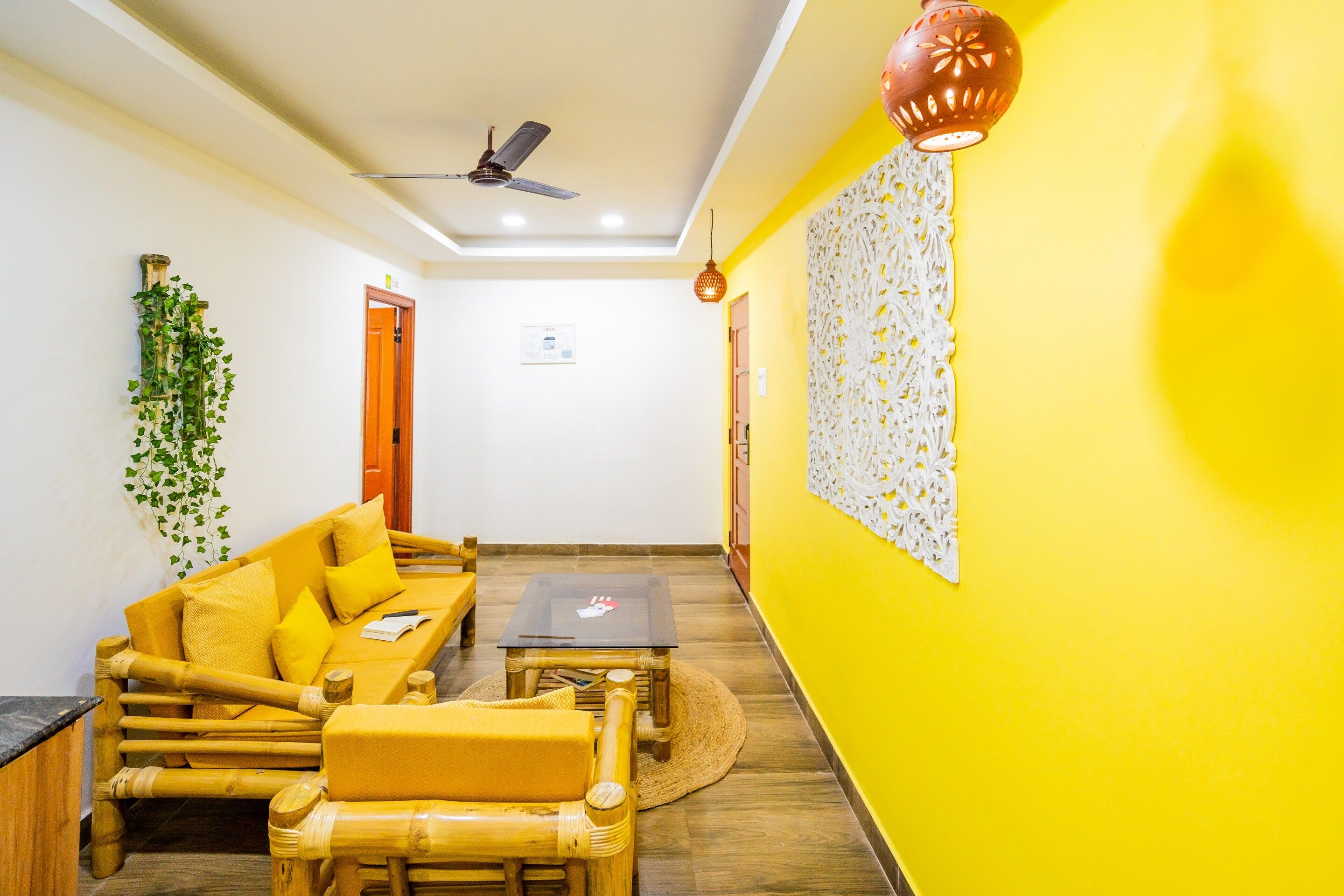 Una stanza con una parete gialla, una ventola a soffitto, un divano con cuscini, un tavolino e un elemento decorativo a parete.