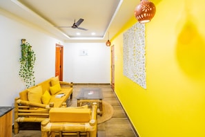 A room with a yellow wall, a ceiling fan, a sofa with cushions, a small table, and a decorative wall piece. - Hotel O Signature Grande (Pondicherry)