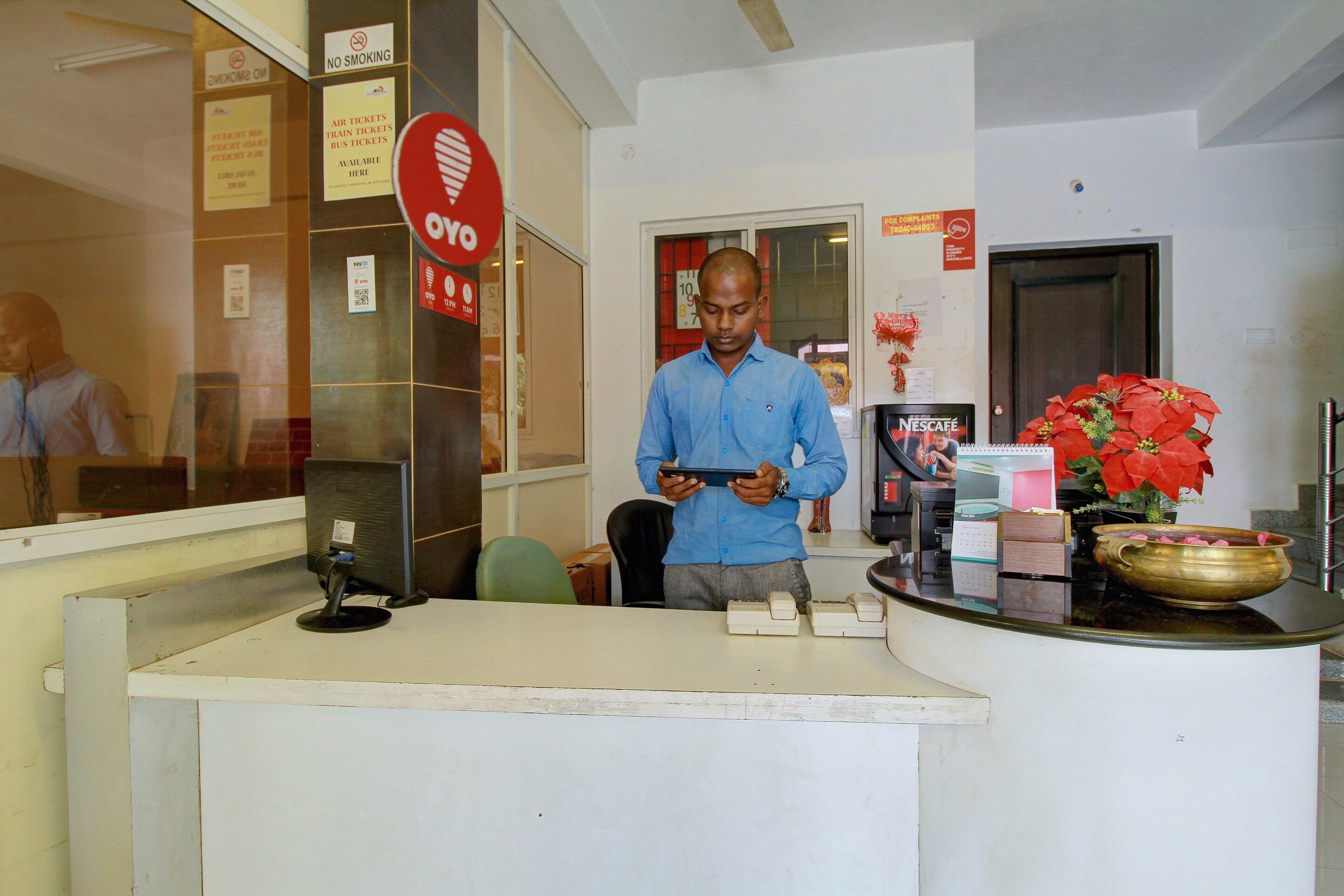 A man at a counter with a computer, a red sign indicating no smoking, and a flower arrangement.