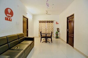 Une chambre d’hôtel avec un canapé, une table à manger avec des chaises, un ventilateur de plafond et une porte portant un numéro.