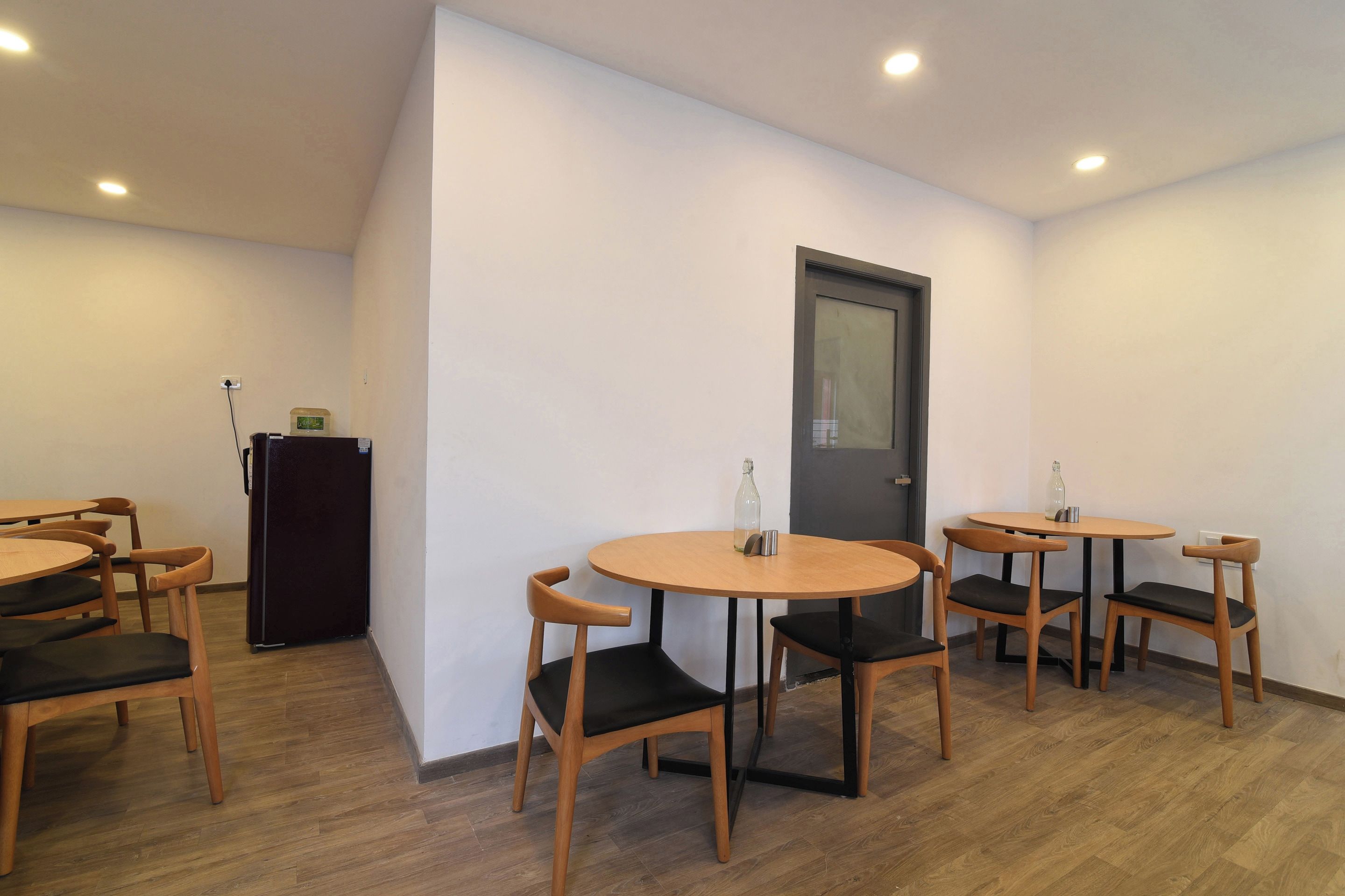 Una habitación con una puerta, un refrigerador y varias mesas redondas con sillas.