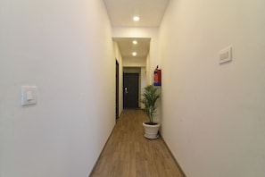 Un pasillo estrecho con suelo de madera, paredes blancas, una planta en maceta, un extintor y una puerta al final.