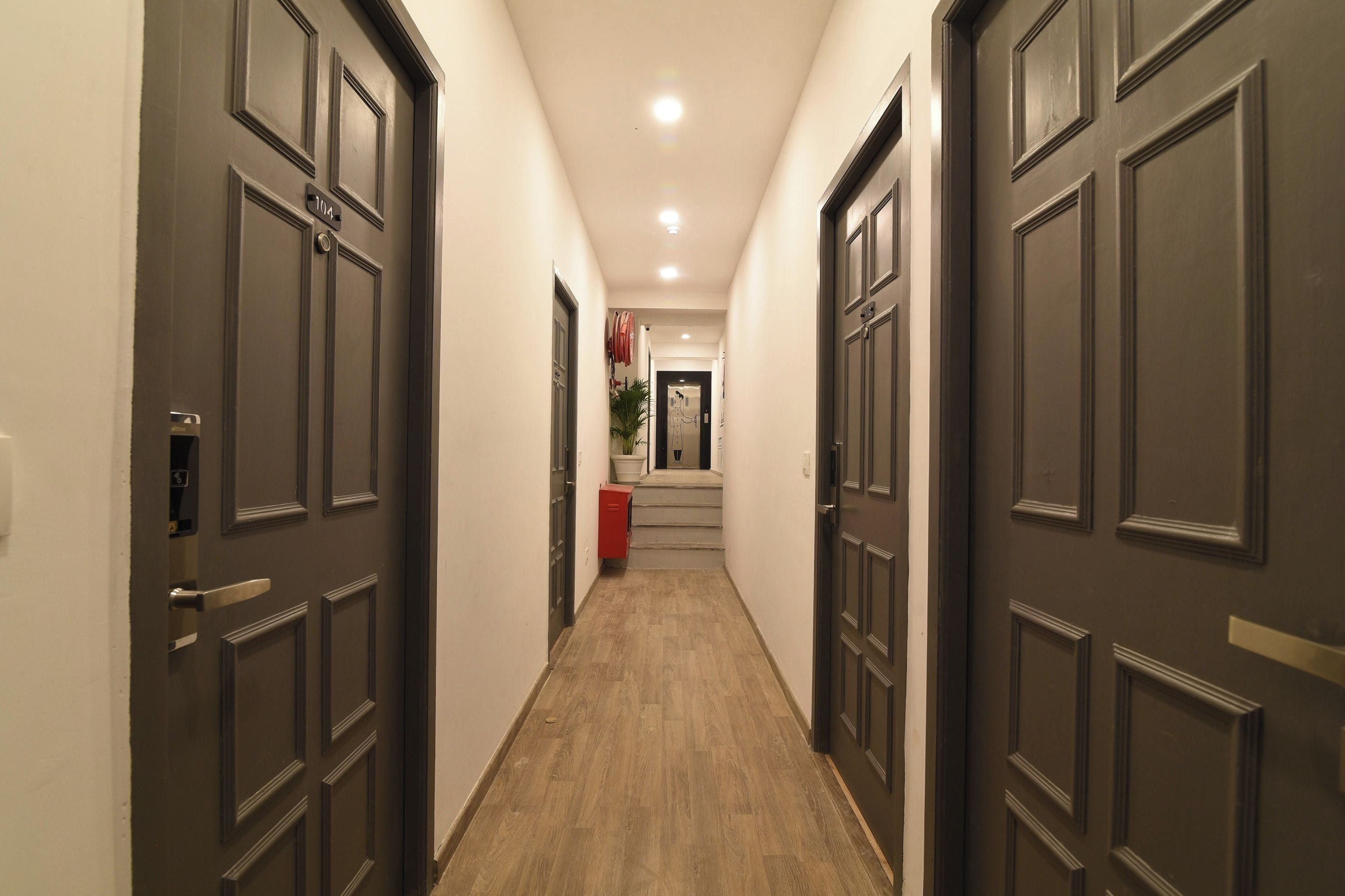 A hallway with dark wooden doors, a wooden floor, and a staircase leading to an elevator.