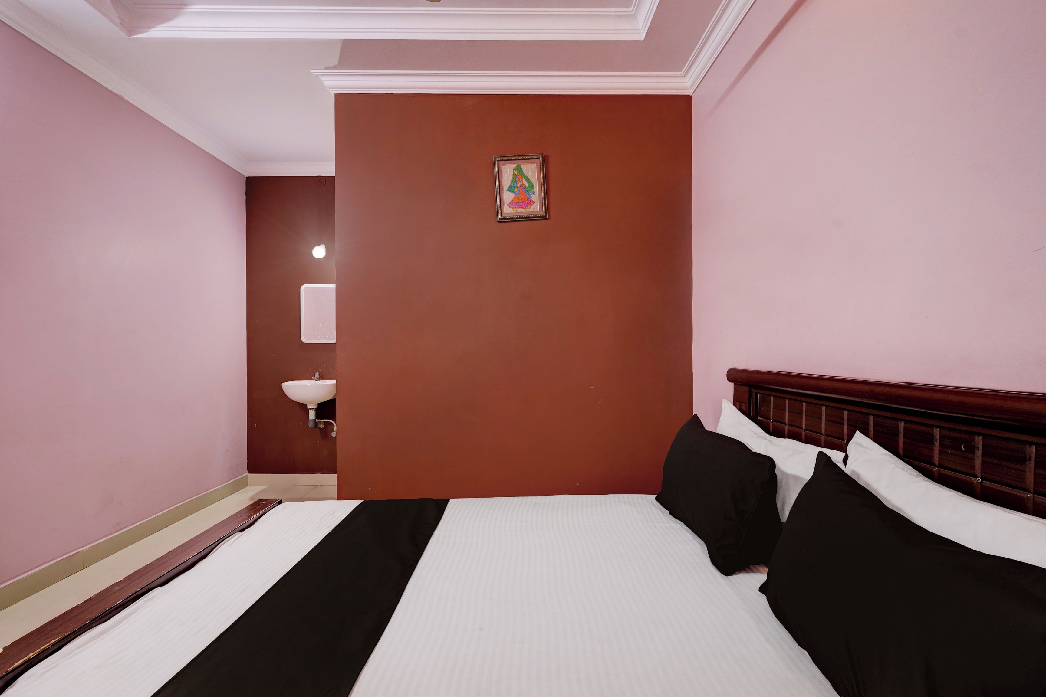 Habitación de hotel con cama, mesita de noche, lavamanos empotrado en la pared y un cuadro enmarcado.