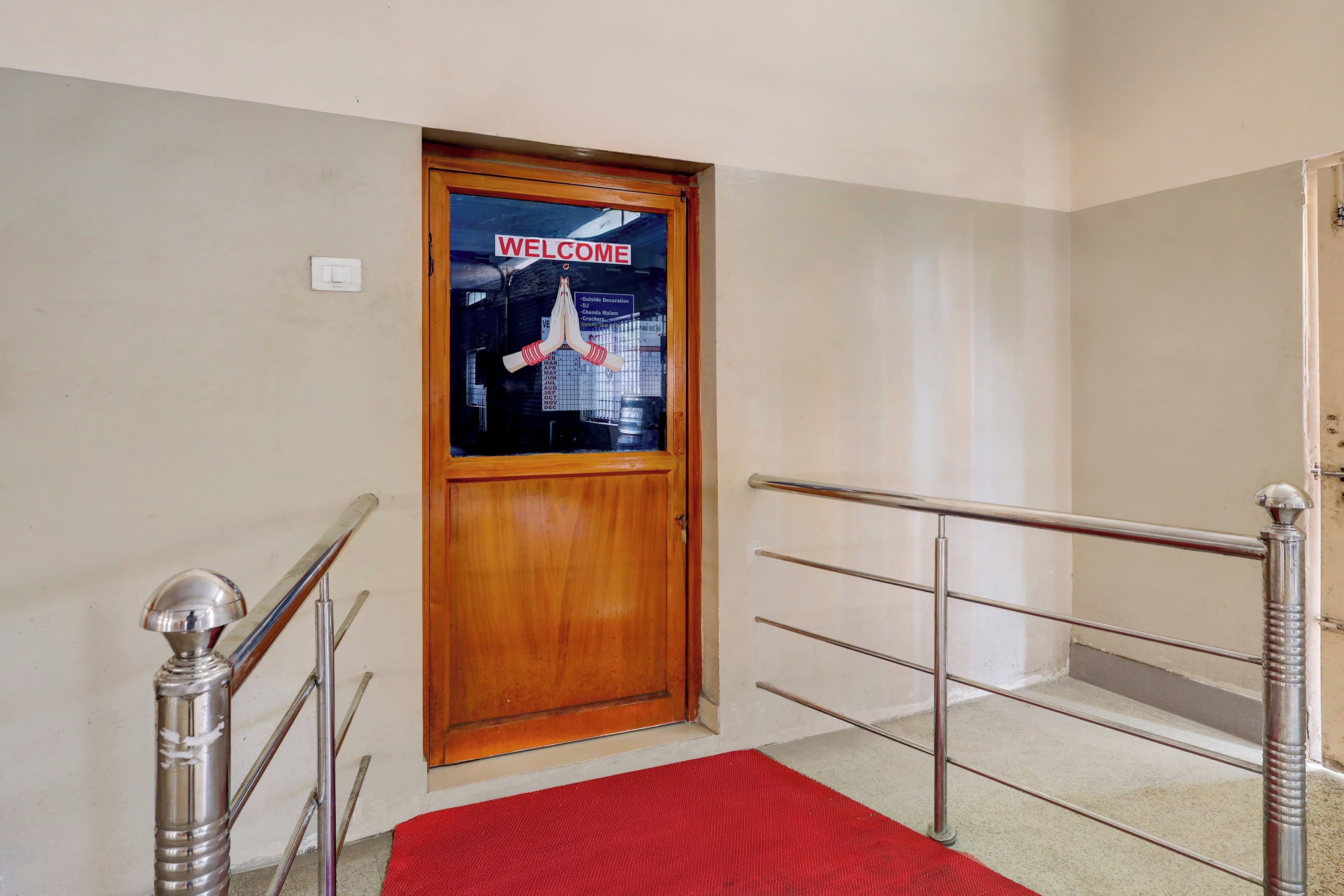 Una puerta de madera con un letrero que dice 'WELCOME', alfombra roja y barandales de metal.