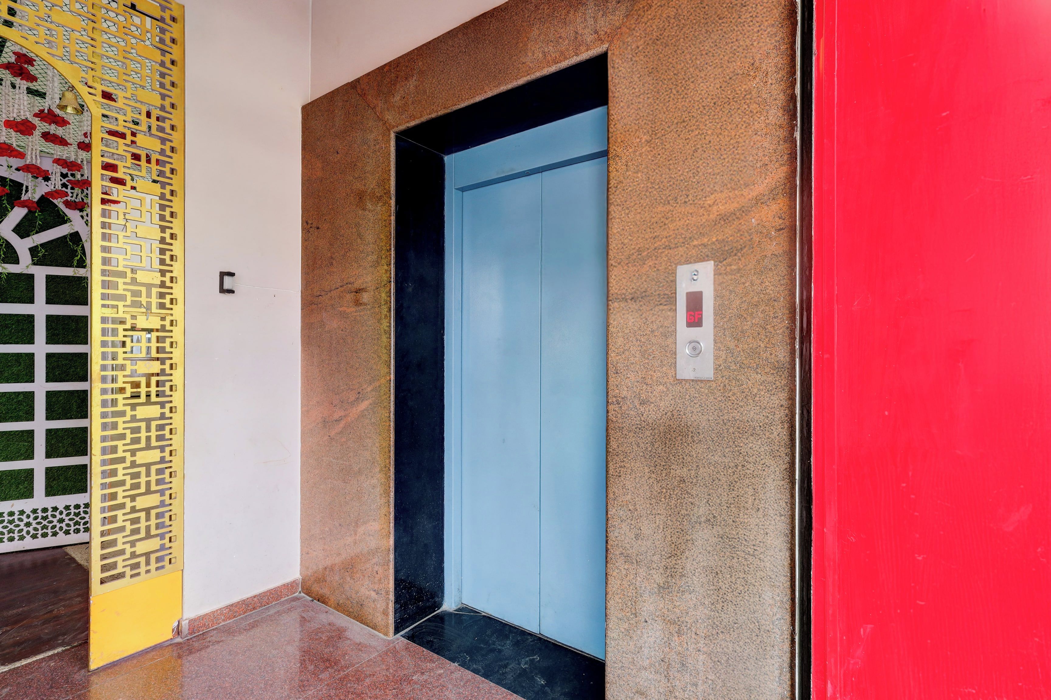 Un ascensore con interni blu, una parete rossa e un pannello decorativo giallo e bianco a sinistra.