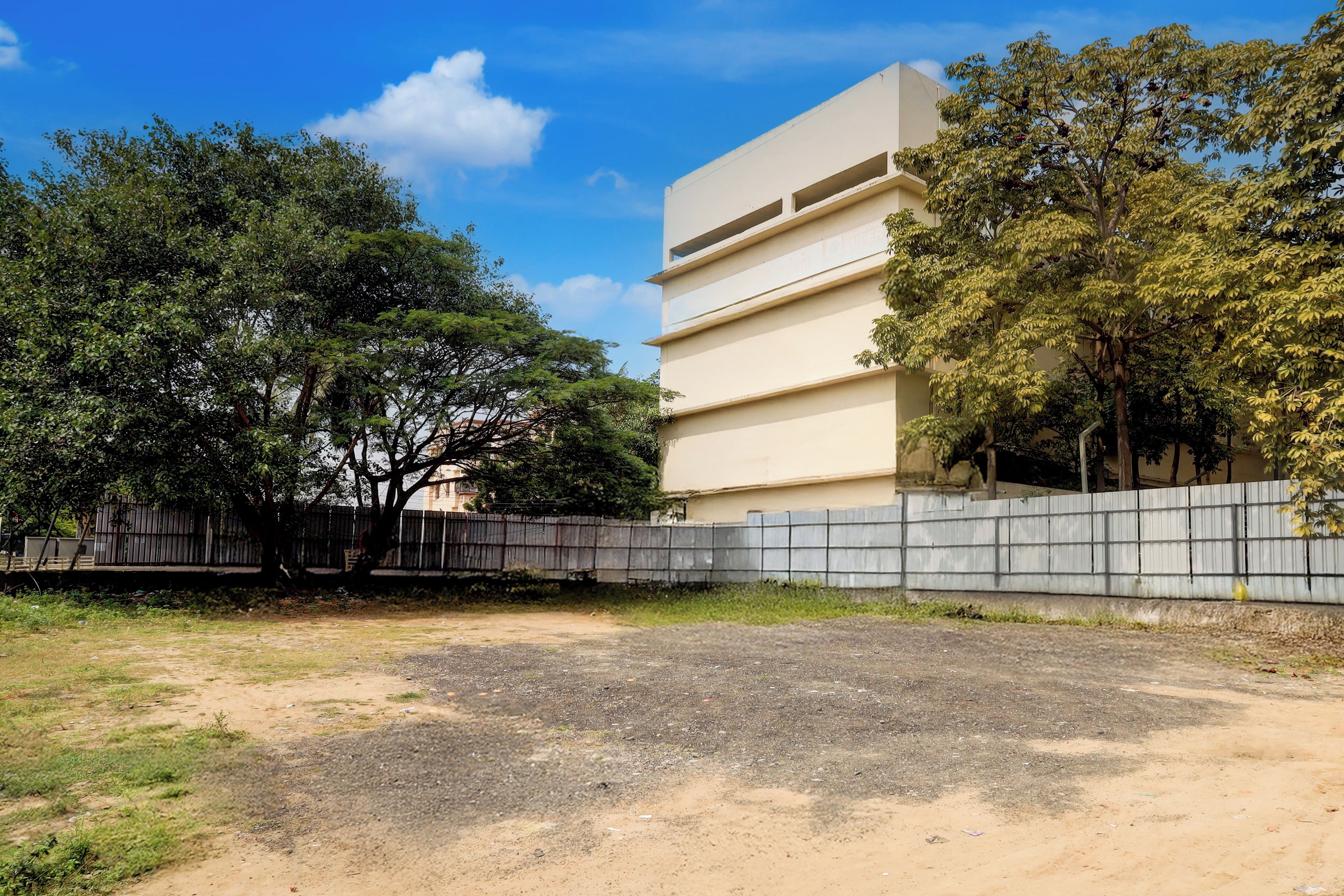 Un edificio con fachada plana y varias ventanas, rodeado de árboles y una cerca.