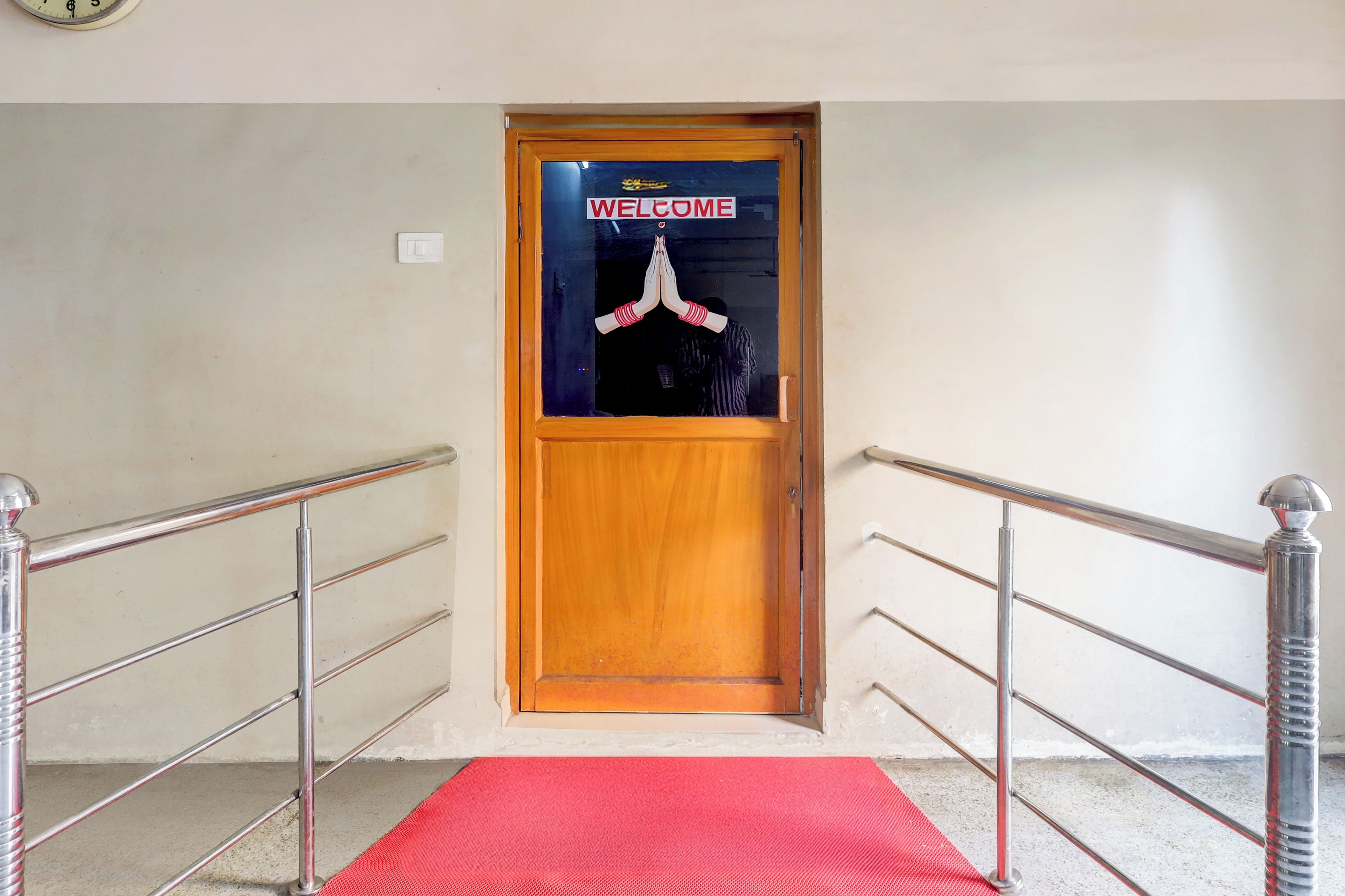 Una puerta de madera con un letrero que dice 'WELCOME', una alfombra roja y barandillas metálicas en una escalera.