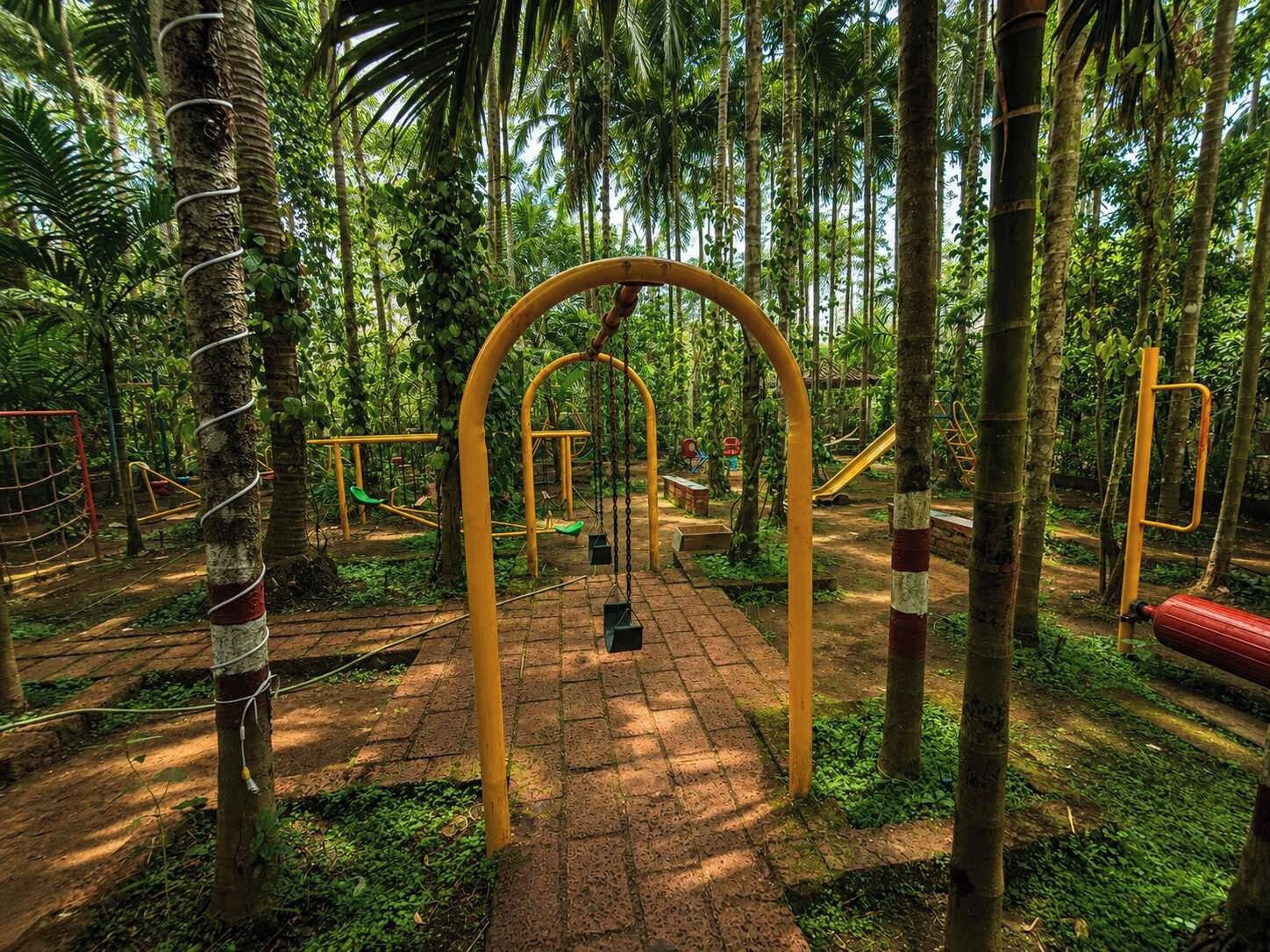 An outdoor playground with swings and climbing structures surrounded by trees.