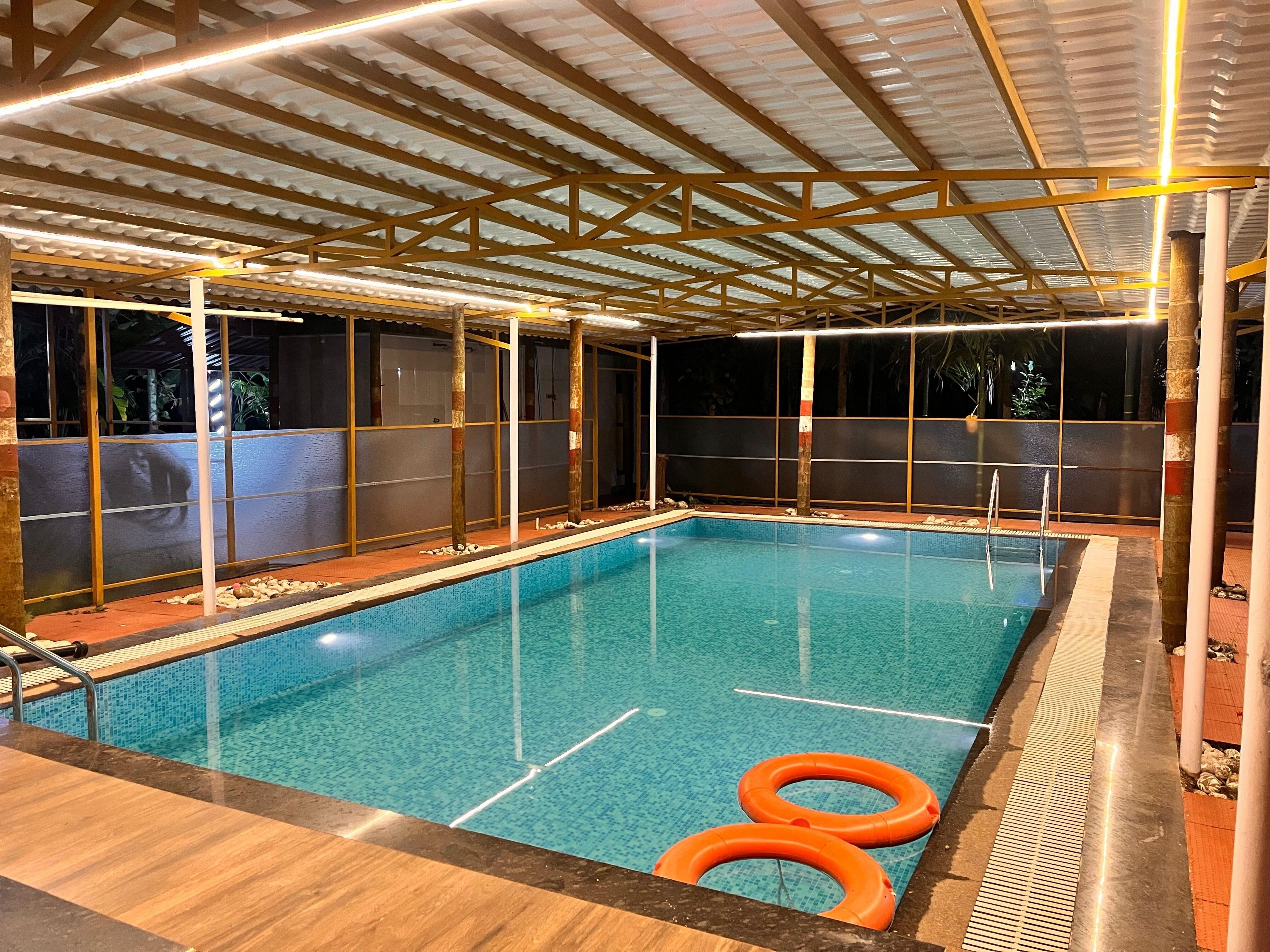 An indoor swimming pool with a tiled floor, surrounded by wooden beams and glass walls.