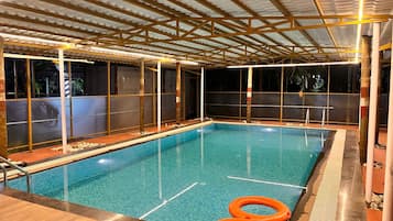 Una piscina interior con suelo de baldosas, rodeada de vigas de madera y paredes de vidrio.