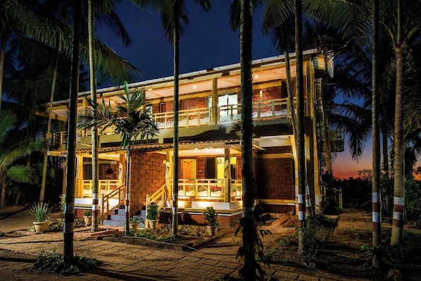 A two-story building with a balcony on the upper floor, surrounded by palm trees.