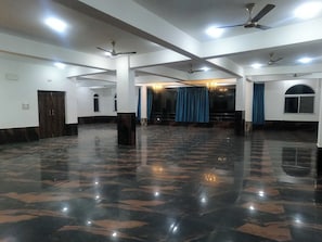 A spacious hall with a polished marble floor, ceiling fans, and a chandelier. - Hotel O K2 (Chakradharpur)