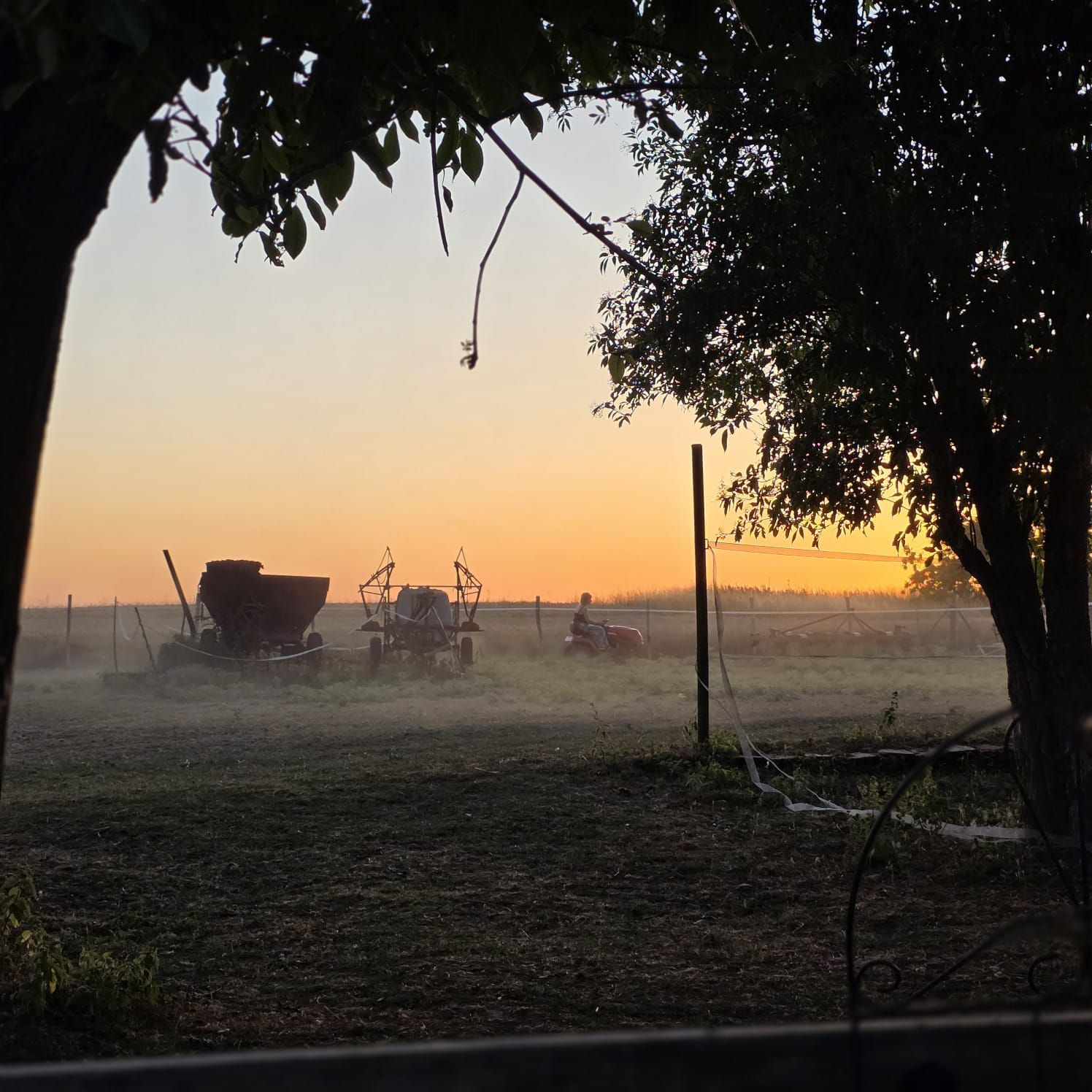 Un paysage rural avec des engins agricoles, une clôture et un arbre au premier plan.