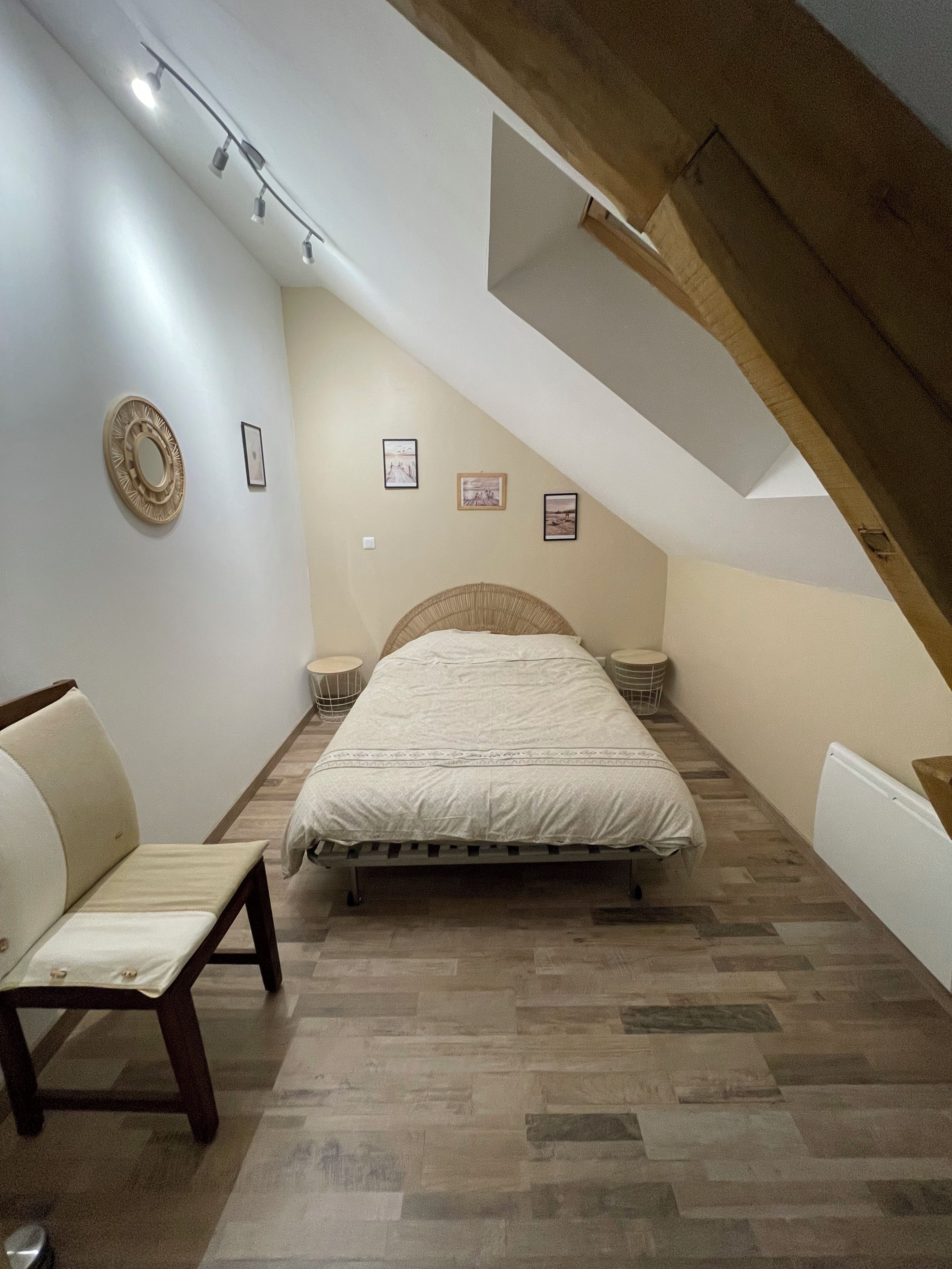 A bedroom with a sloped ceiling, a bed, a bench, and a wall-mounted light fixture.
