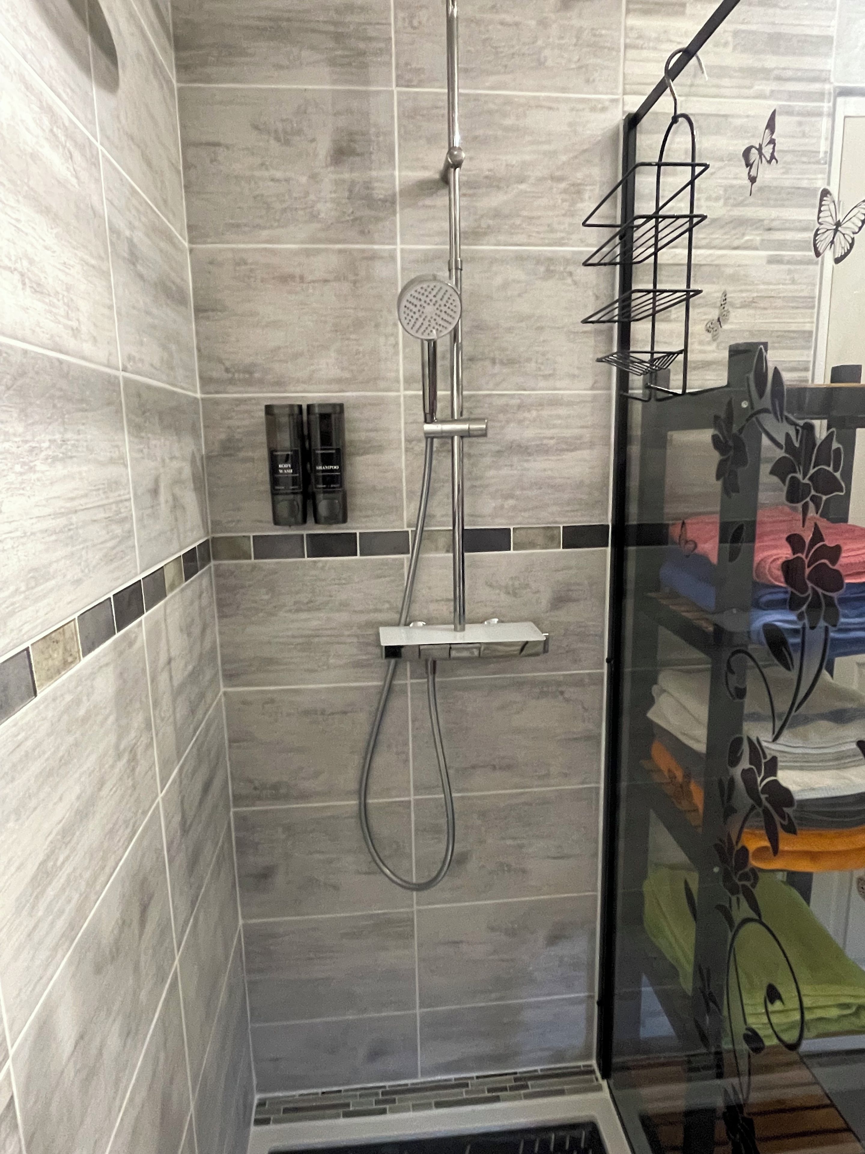 Een douche met een handdouche en een douchecabine met glazen wanden en een plankje.