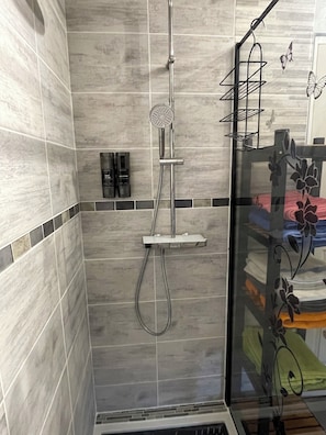 A shower with a handheld showerhead and a glass-enclosed shower area with a shelf.