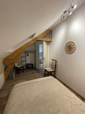 Une chambre avec un plafond en pente, un lit recouvert d’une couvre-lit à motifs, une chaise, une petite table et un élément décoratif mural.