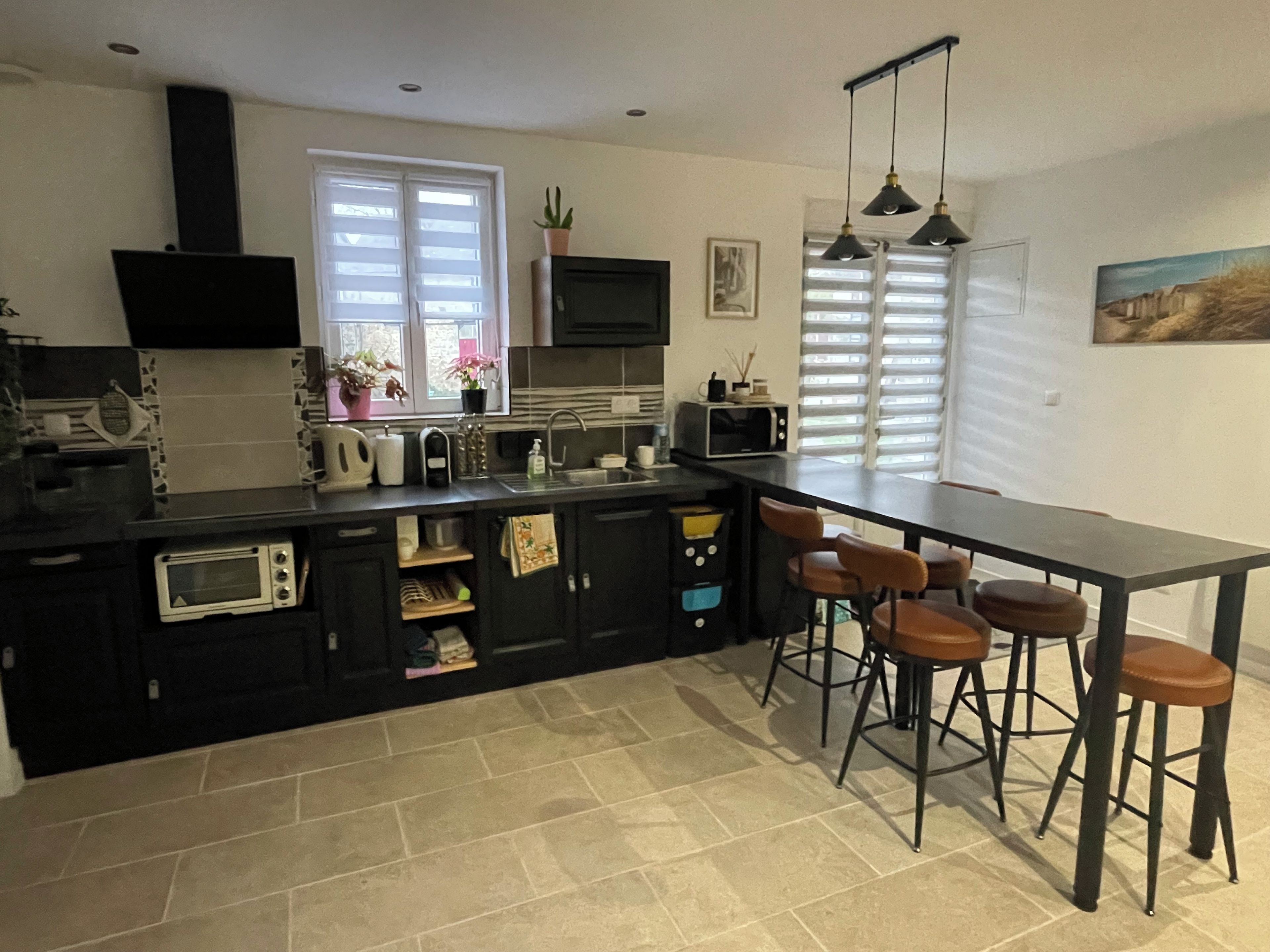 Een moderne keuken met een zwart aanrecht, witte kasten, een ingebouwde magnetron en een bar met barkrukken.