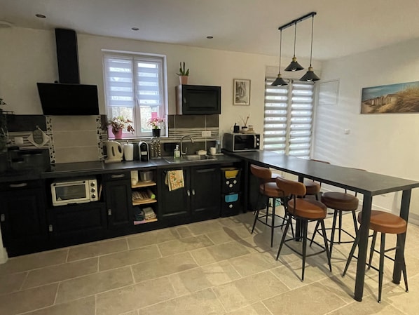 A modern kitchen with a black countertop, white cabinets, a built-in microwave, and a bar area with stools.