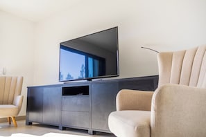 Un salon moderne avec un téléviseur à écran plat fixé sur un meuble sombre, un fauteuil beige et un canapé.