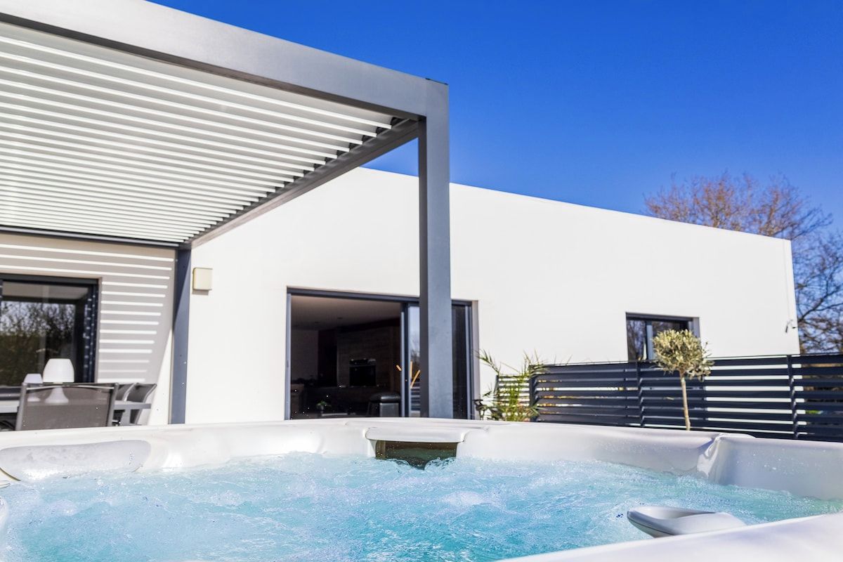 Un espace moderne aménagé à l’extérieur avec un jacuzzi, un ciel dégagé, un bâtiment blanc et une terrasse avec des sièges.