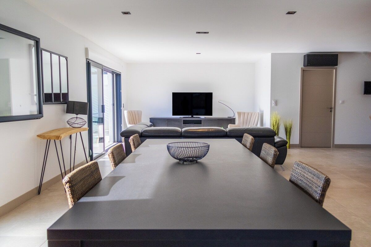 Un salon moderne doté d’un grand téléviseur à écran plat, d’une table à manger avec des chaises et d’un ensemble de canapés.