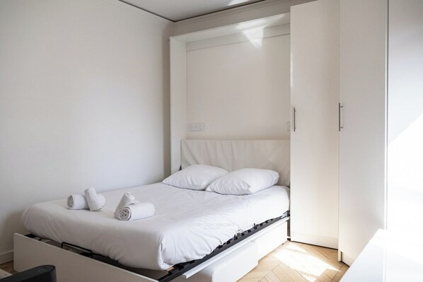 Una camera da letto minimalista con un letto, un armadio e un comodino.