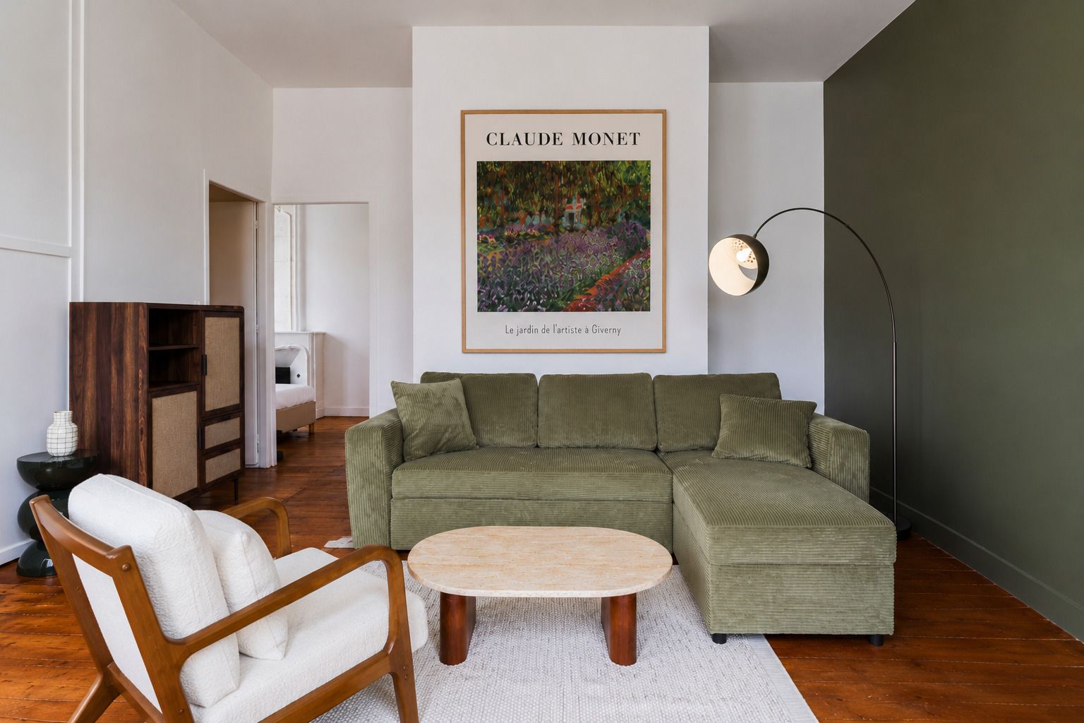 Una sala de estar con un sofá verde, una silla de madera, una mesa de centro redonda y una obra de arte enmarcada en la pared.