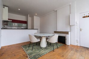 Un espacio habitable compacto con una mesa de comedor redonda, cuatro sillas, una zona de cocina con armarios y una chimenea.
