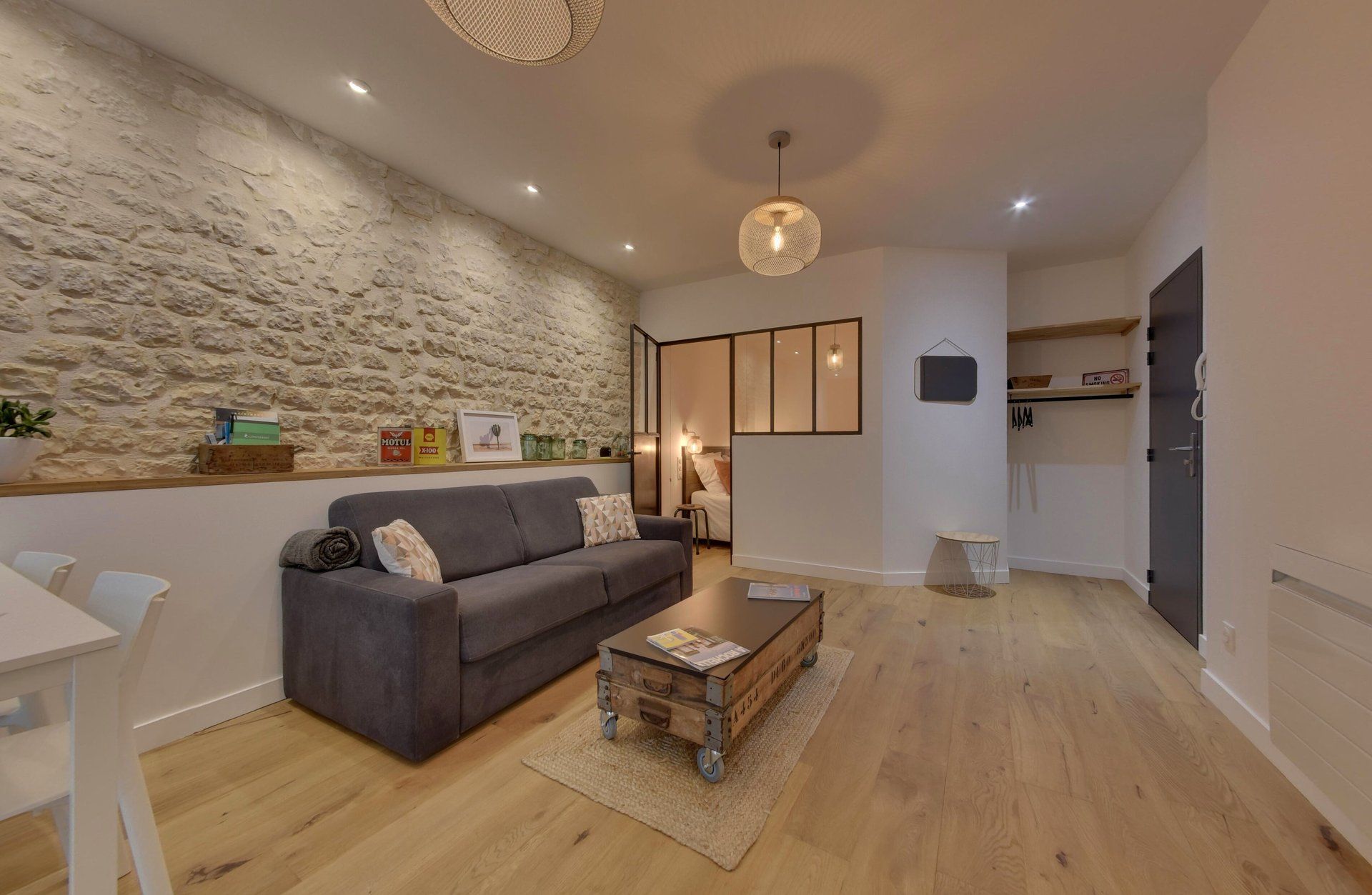 Een moderne woonkamer met een stenen muur, een grijze bank, een houten salontafel en een kleine eettafel.