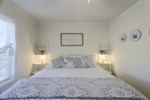 Une chambre à coucher avec un lit, deux lampes de chevet, une fenêtre avec des stores et un tableau accroché au mur.