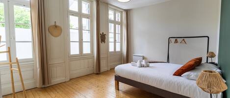 A bedroom with a bed, a standing lamp, and a window with curtains.