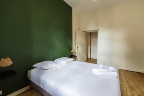 Una camera d'albergo con un letto, un comodino, una lampada e una porta che dà su un'altra stanza.