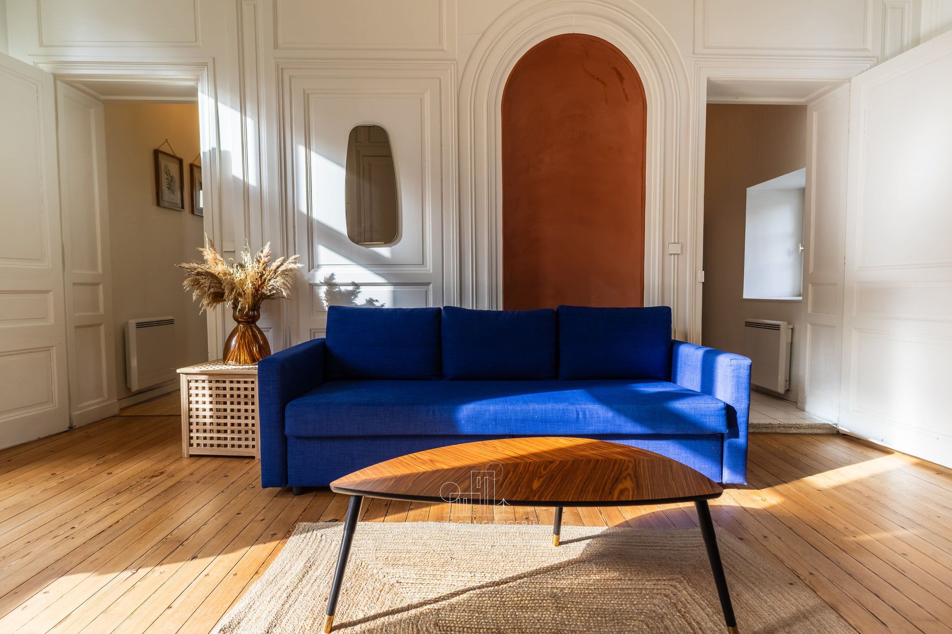 Una stanza con un divano blu, un tavolino in legno e un vaso con piante essiccate.