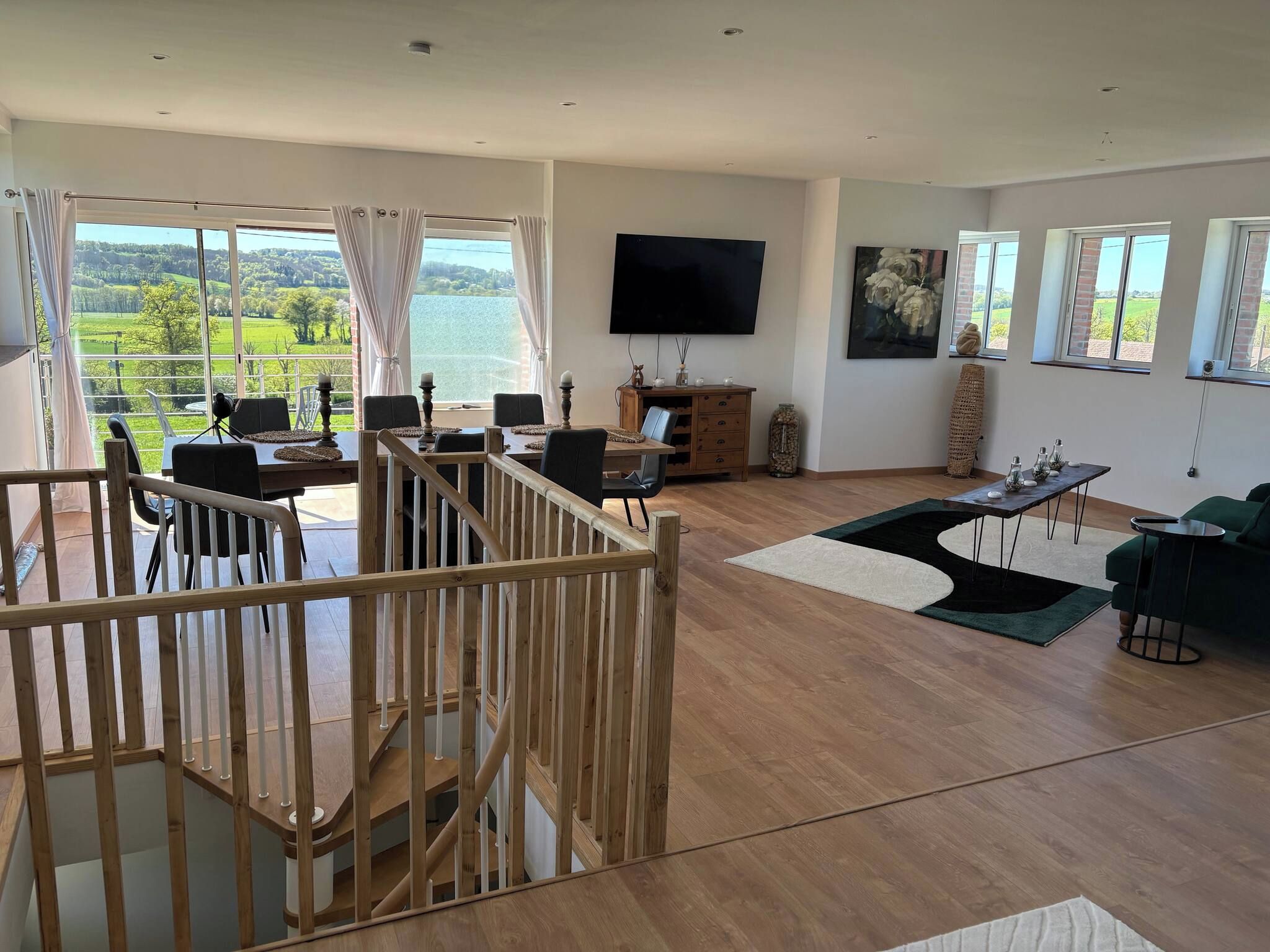 A spacious living area with a wooden staircase, a dining table, and a view of a lake.