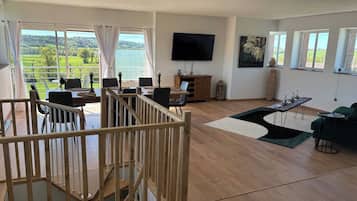 A spacious living area with a wooden staircase, a dining table, and a view of a lake.