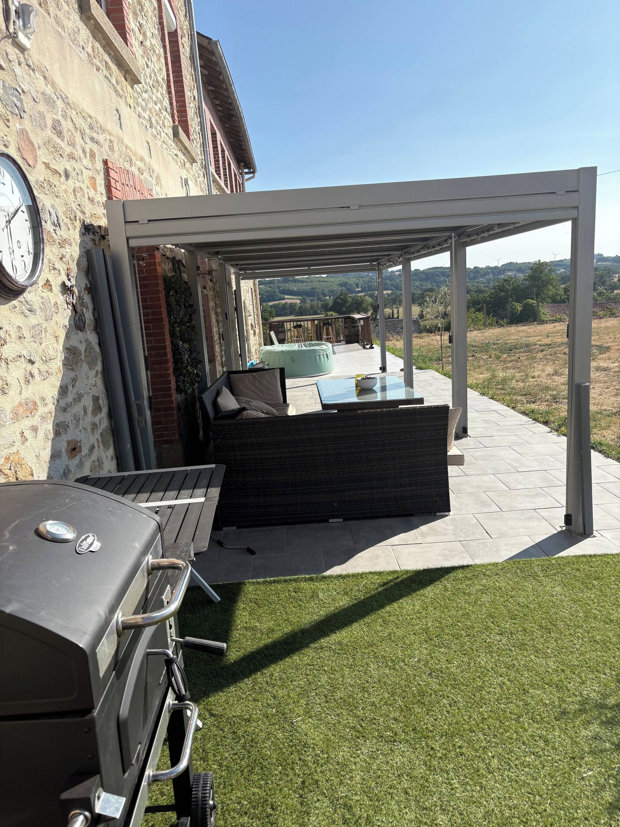 Un patio exterior con una parrilla, asientos y vistas al campo.