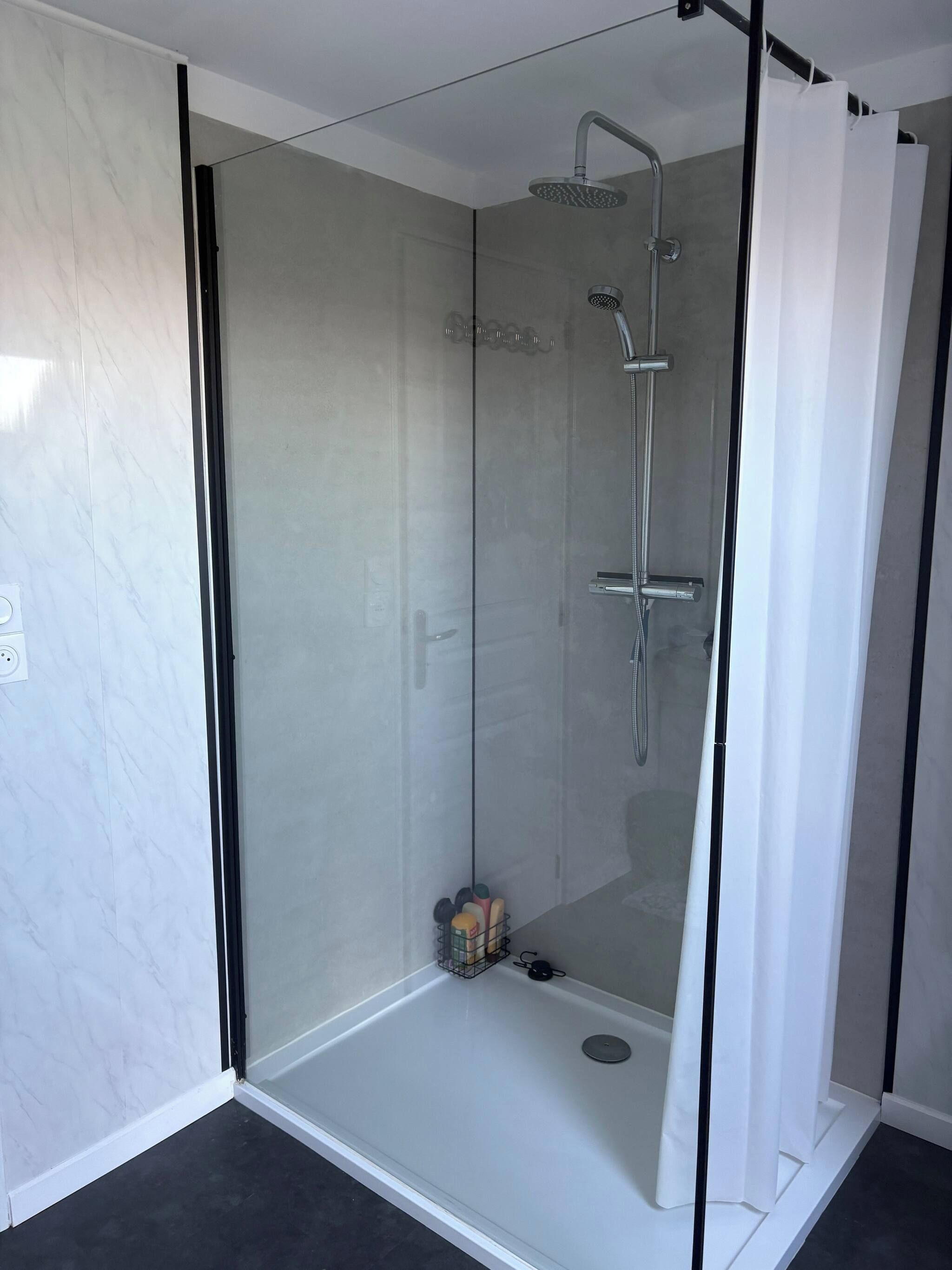 Une cabine de douche fermée par des parois en verre, dotée d’un pommeau de douche à main et d’un robinet mural.