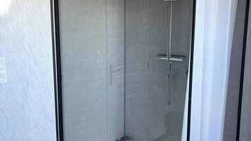 Une cabine de douche fermée par des parois en verre, dotée d’un pommeau de douche à main et d’un robinet mural.