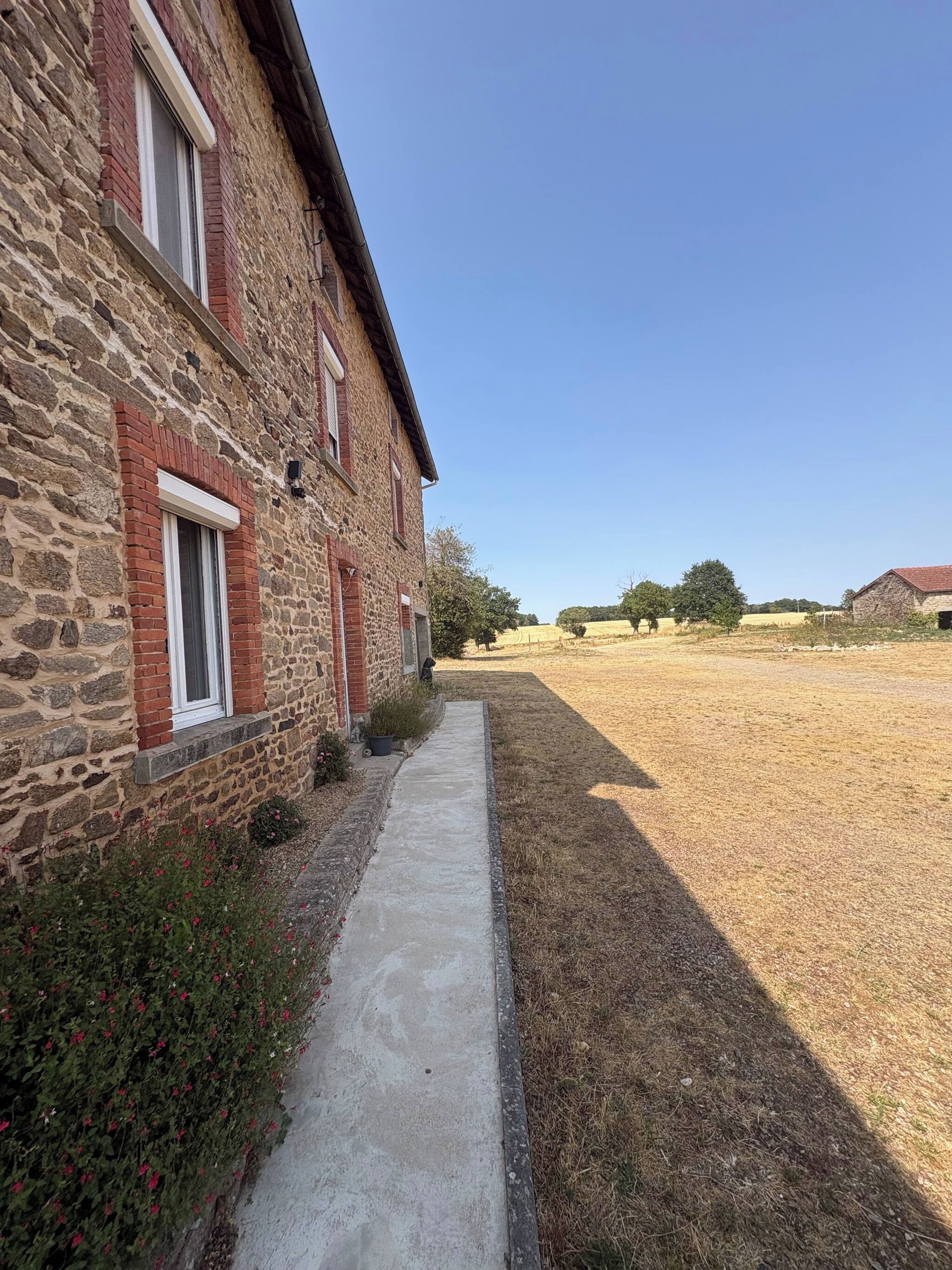 Un bâtiment en pierre avec un chemin en béton menant à un champ.