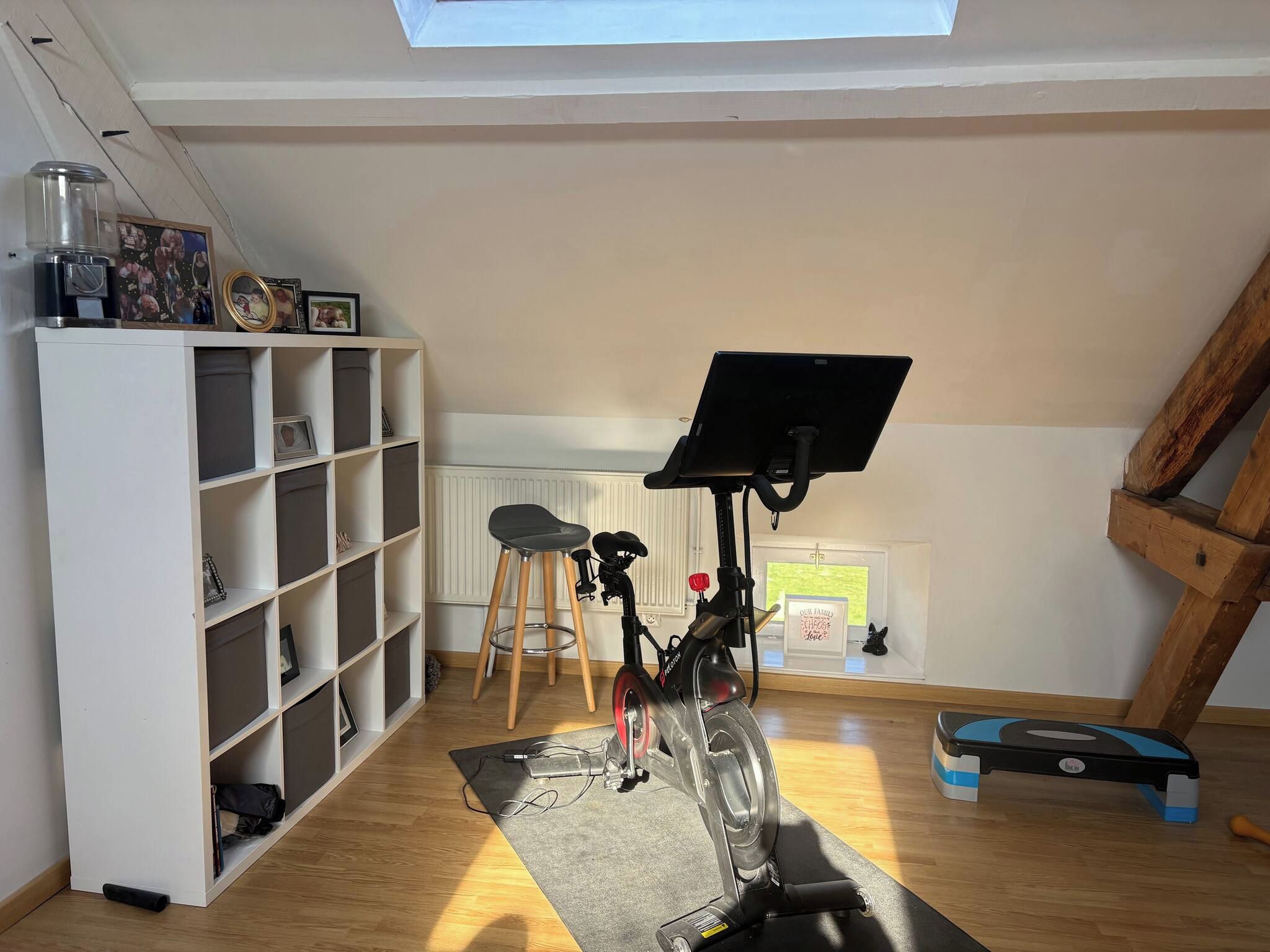 Een kamer met een plafondventilator, een witte plank met foto's, een bureau met een laptop, een fiets en een raam met uitzicht.